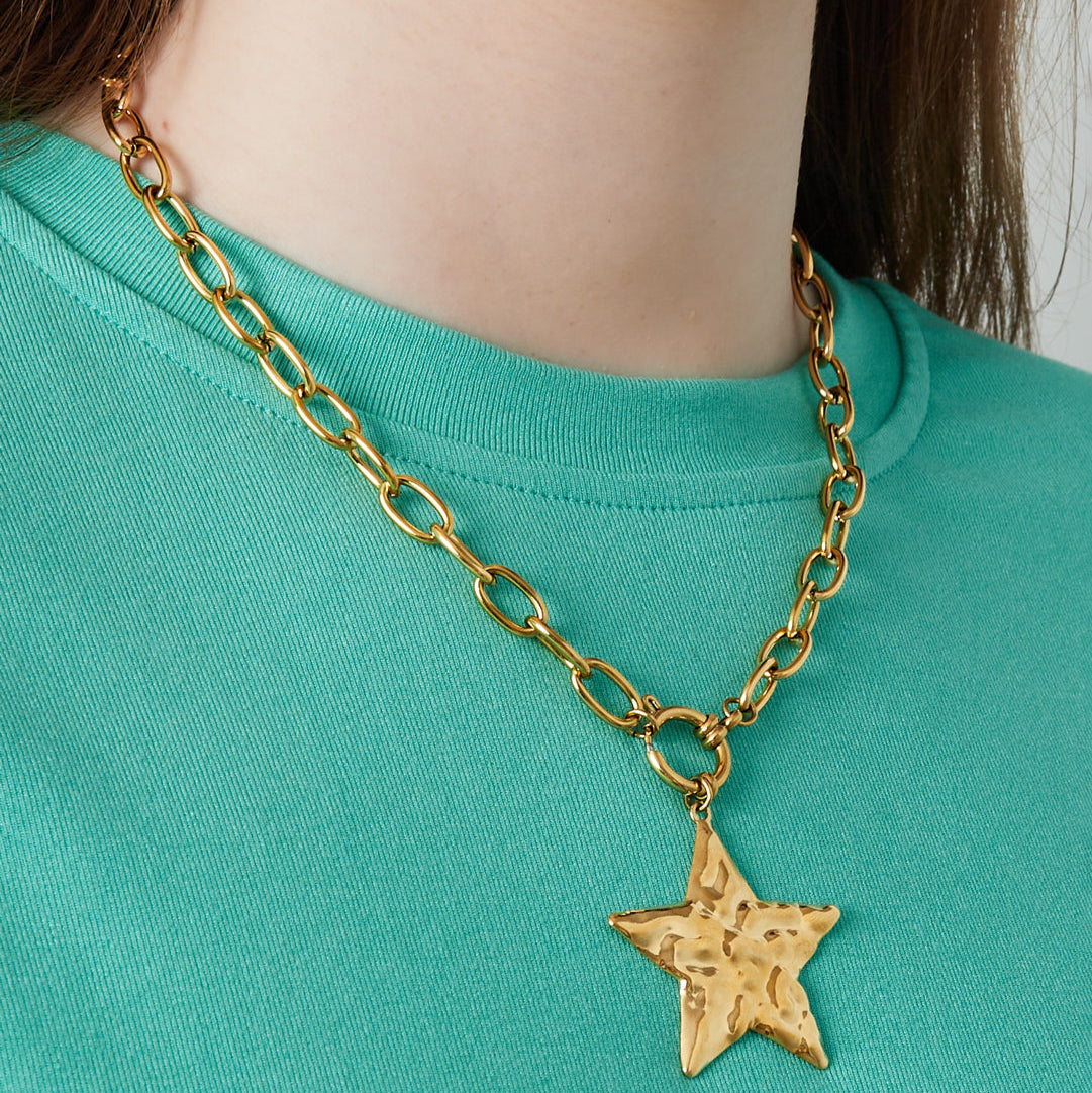 Gold chain necklace with a star pendant worn by a person in a green shirt.