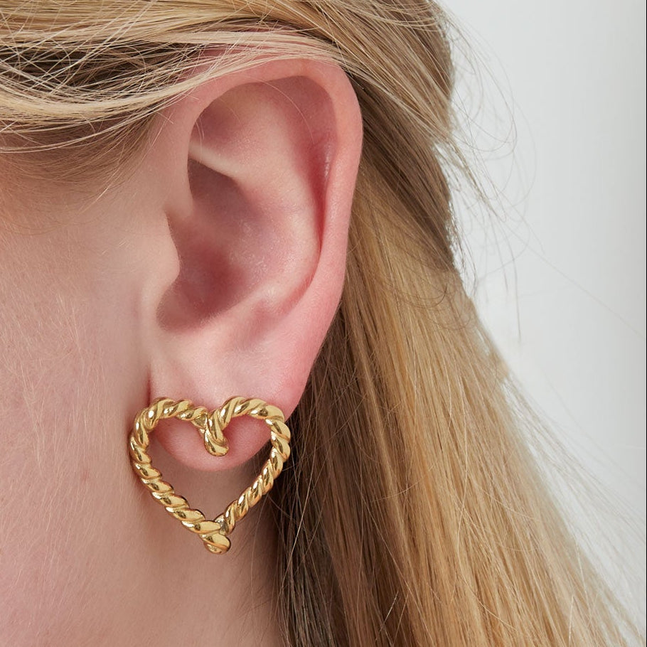 Gold heart-shaped earring worn by a person with blonde hair.