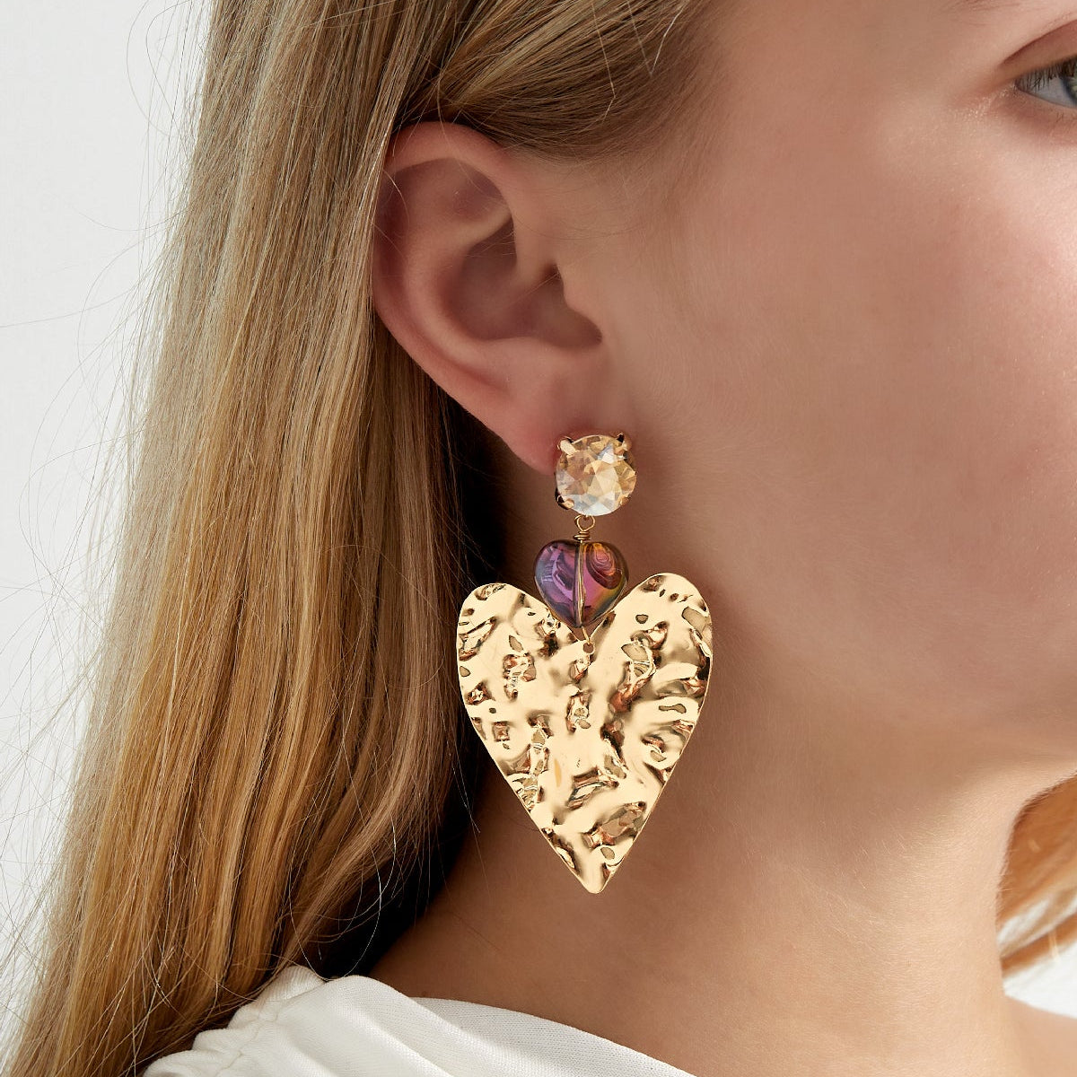 Close-up of a person wearing gold heart-shaped earrings with multicolored stones.