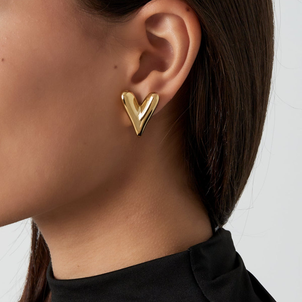 Gold heart-shaped earring worn by a person with a plain background