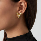 Gold heart-shaped earring worn by a person with a plain background