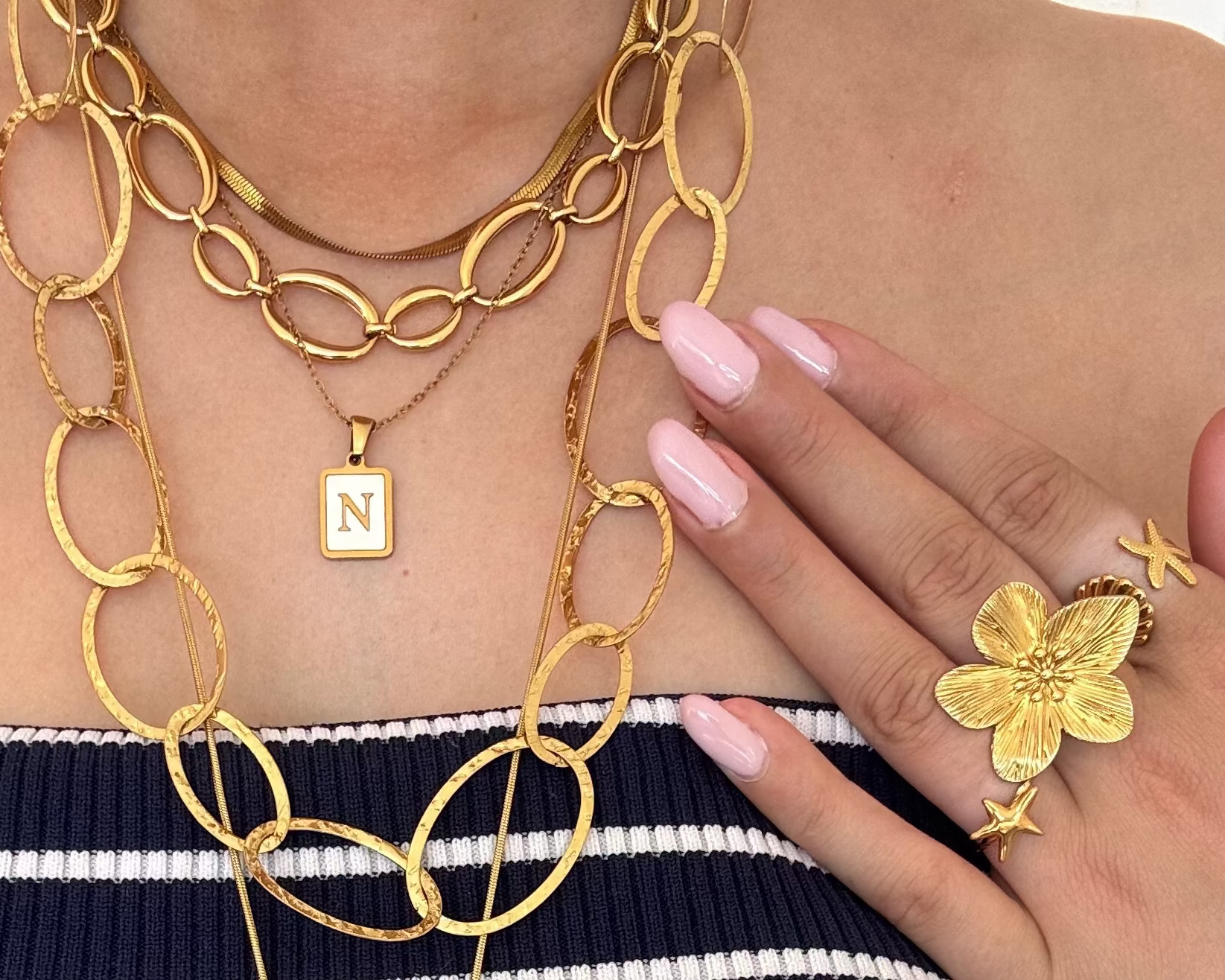 Gold chain necklace with a pendant and matching ring on a person wearing a striped garment.