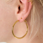 Gold hoop earrings worn by a person with blonde hair. bynooni bynooni.nl