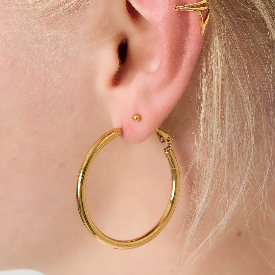 Gold hoop earrings worn by a person with blonde hair. bynooni bynooni.nl