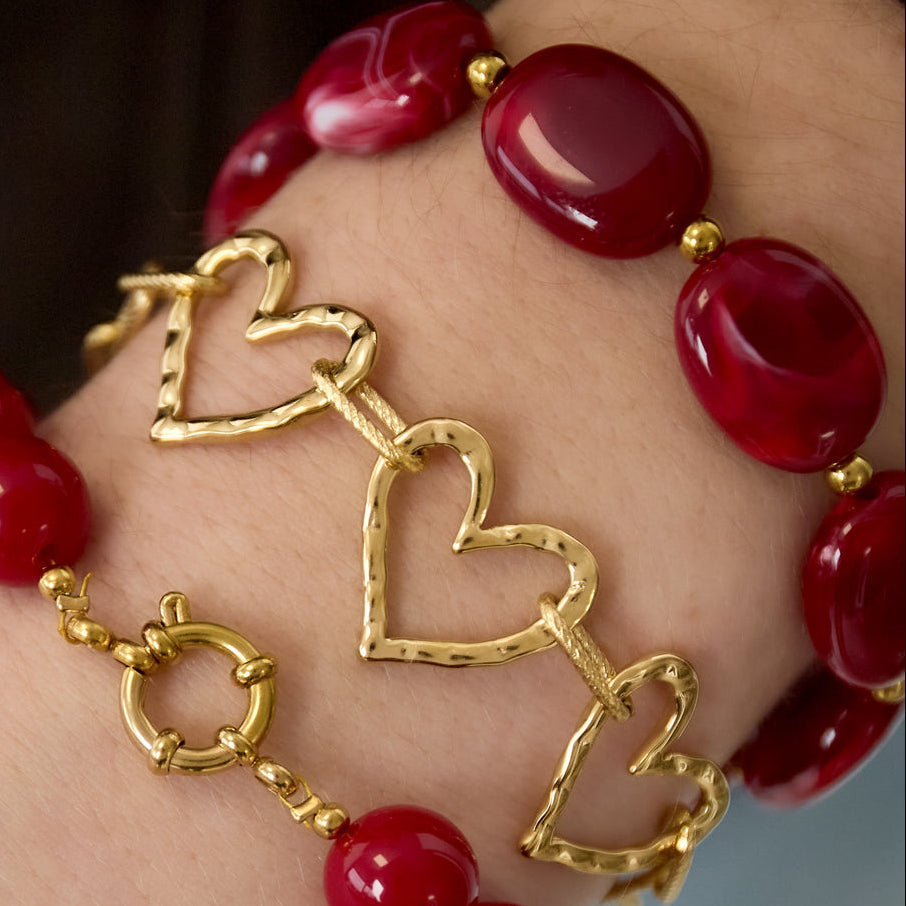 Bracelet with red beads and gold heart-shaped charms on a wrist.