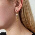 Close-up of a person wearing a gold earring with heart and bead design.