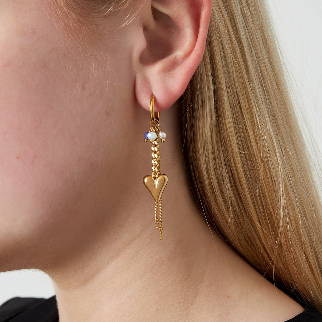 Close-up of a person wearing a gold earring with heart and bead design.