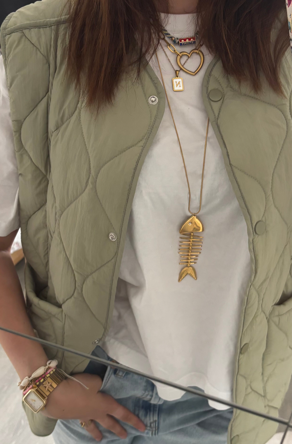 Person wearing a green quilted vest, white shirt, and gold necklace with a fish design.