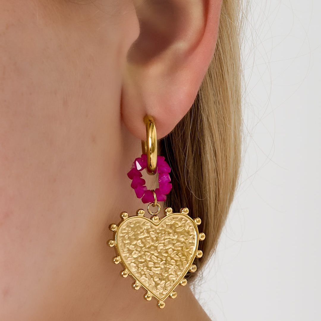 Gold heart-shaped earring with pink beads worn by a person on a white background