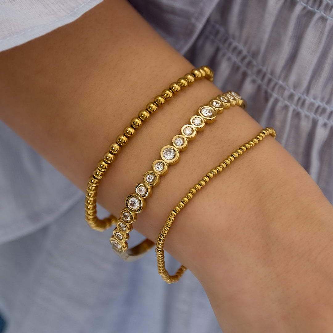 Gold bracelets on a person's wrist with a blurred background
